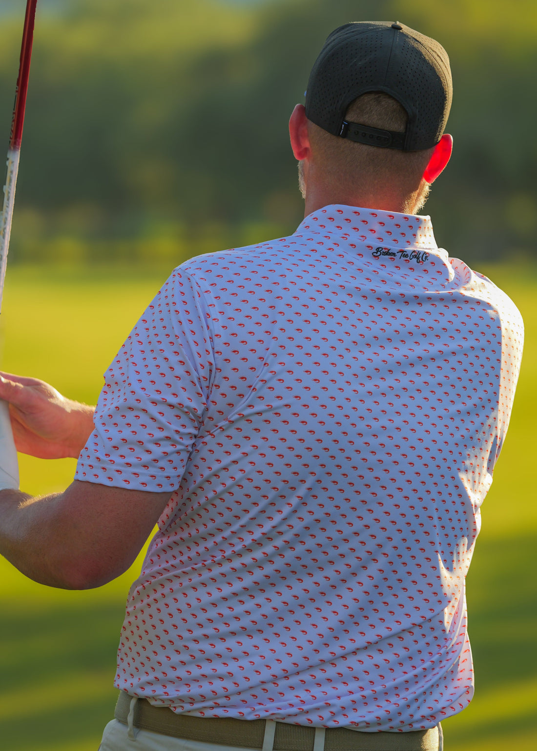 Man in a patterned shirt and cap holding a golf club on a golf course