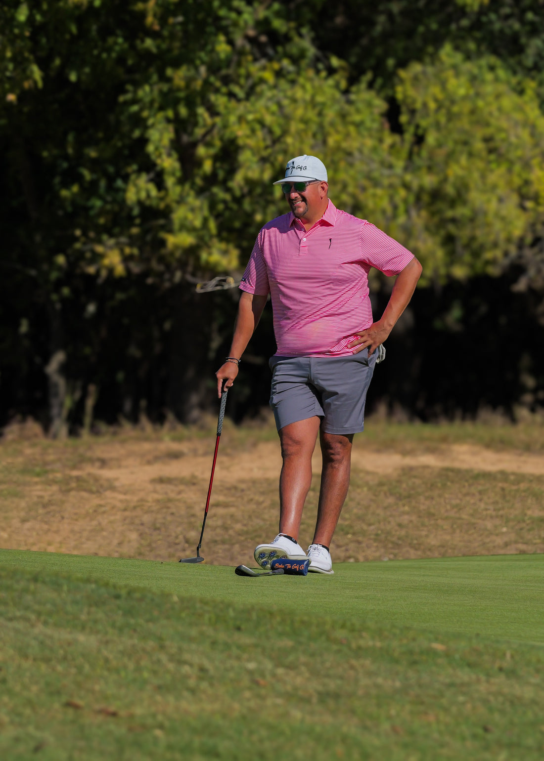 Man in red stripes shirt and gray shorts playing golf on a green course with trees in the background